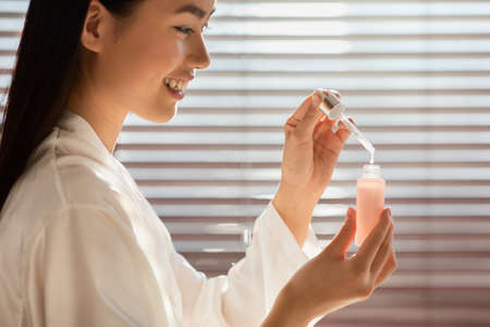 Side view of woman holding bottle with serum