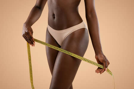 Unrecognizable dark skinned woman holding measuring tape over her legsの写真素材