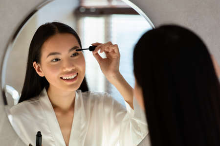 Beautiful chinese lady applying makeup in bathroomの写真素材