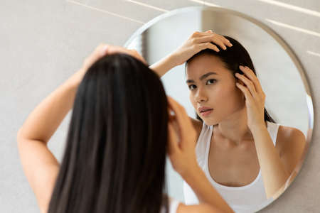 Upset long-haired japanese woman checking her hairの写真素材