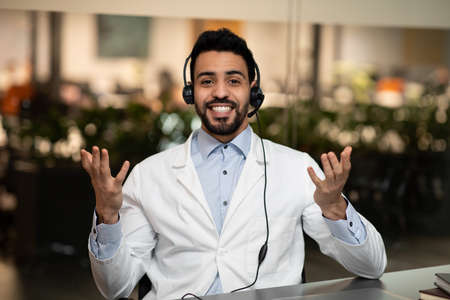 Smiling young handsome middle eastern engineer or doctor in headphones gestures, look at cameraの写真素材