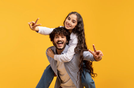 Romantic indian couple having fun together, showing V-sign gesture, guy piggybacking his girlfriend,...