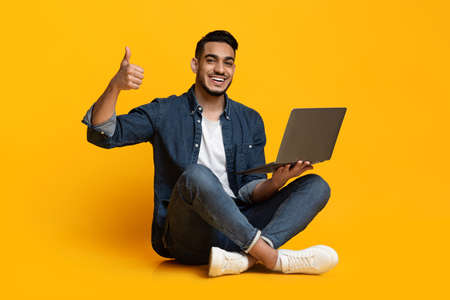 Cheerful arabic guy with laptop showing thumb up