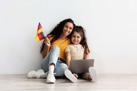 Happy Arab Mom And Little Daughter Holding Laptop And Flag Of Germanyの写真素材