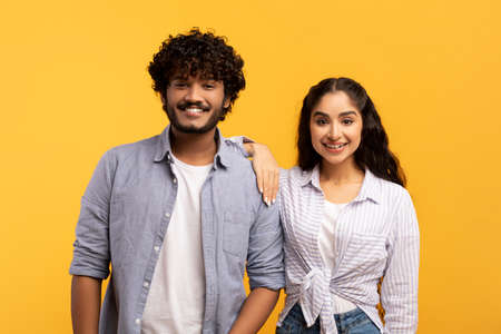 Happy millennials. Portrait of romantic indian spouses posing over yellow background and smiling at...