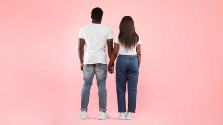 Confident couple standing abck to camera at pink studio background