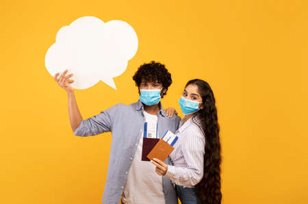 Indian couple wearing face masks, ready to travel abroad, woman holding passports, man holding empty...