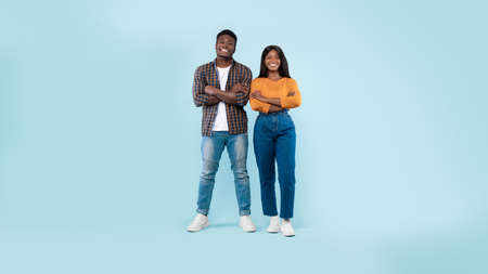 Confident couple standing with folded arms at blue studio background