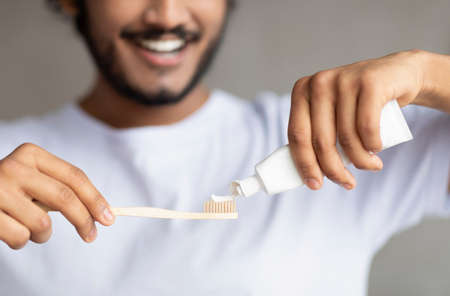 Morning time, personal oral hygiene and dental care. Young bearded man squeezing toothpaste on toothbrushの写真素材