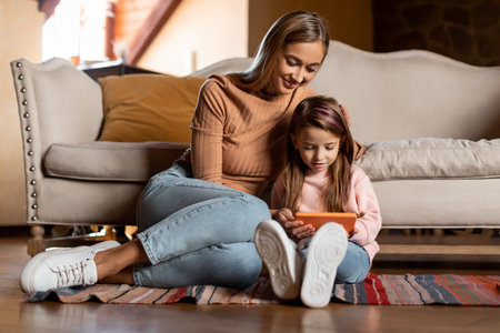 Portrait of smiling mom and daughter using smartphone at homeの写真素材