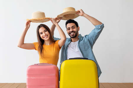 Family vacation. Happy tourist couple taking off hats with greeting gesture standing behind suitcase luggagesの写真素材