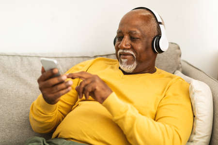 Senior Black Male Listening Music On Phone Wearing Headphones Indoorの写真素材