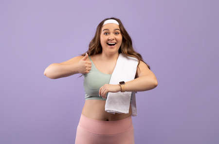 Cheerful cute excited caucasian plus size young female in sports uniform with fit tracker show thumb...