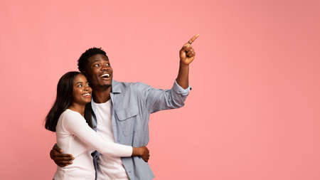 Happy african american couple embracing and pointing at copy space