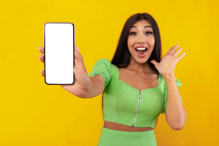 Excited woman showing white empty smartphone screen in hand