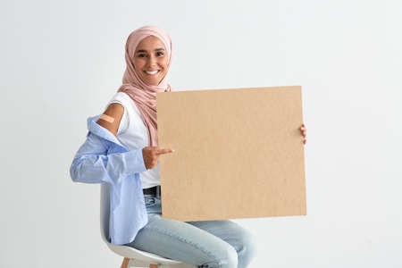 Vaccination Campaign. Muslim Lady In Hijab Pointing At Blank Board In Hands
