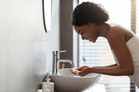 African american lady washing face in bathroomの写真素材