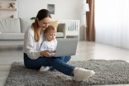 Young mother and her toddler son using laptop computer, surfing internet or shopping online at home, free spaceの写真素材