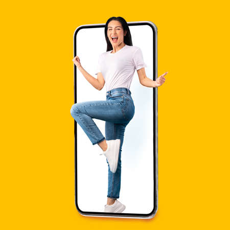 Happy emotional millennial european woman with open mouth screaming at empty screen of huge phone,...