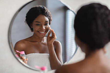 Cheerful pretty black lady using micellar waterの写真素材
