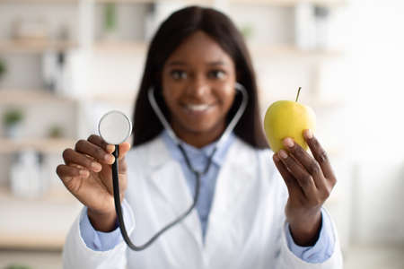 African american nutritionist showing organic green apple and using stethoscope, closeupの写真素材