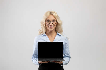 Happy young businesswoman holding laptop computer with blank screen for your ad or website design