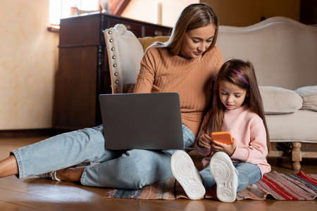 Happy woman and daughter using laptop and cellphone