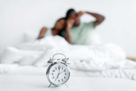 Sleepy young african american man and woman wake up after sleep rubbing eyes on bed with white soft blanketの写真素材
