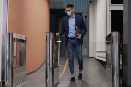 Man in face mask holding laptop, passing through entrance gate