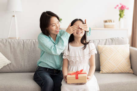 Mature Asian woman covering her granddaughters eyes, making surprise birthday gift at homeの写真素材