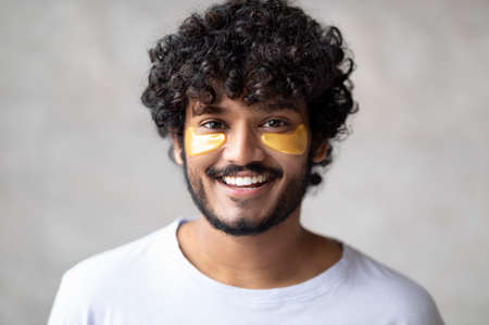 Modern beauty products. Portrait of handsome indian man with golden patches under eyes posing in...