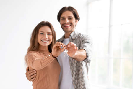 Cheerful young european guy and woman hold key in hands together on window background in roomの写真素材
