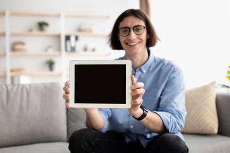 Happy young man holding modern digital tablet with empty blank screen, digital device with mockup...