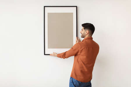 Young man hanging picture frame on the wallの写真素材