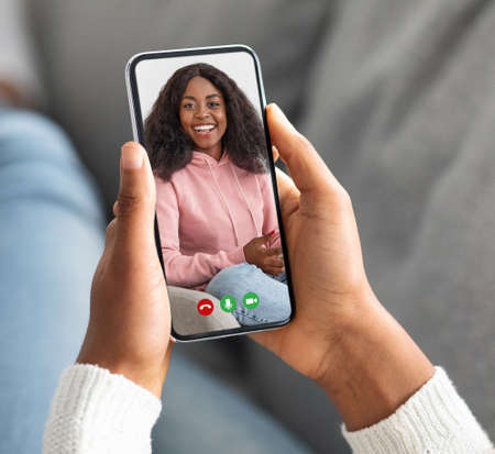Black lady holding cellphone and making video call with her bestie, resting at home on sofa, closeup, creative collageの写真素材