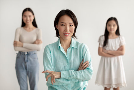 Beautiful mature Asian woman with her adult daughter and granddaughter posing with crossed arms and smiling at cameraの写真素材