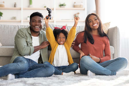 Joyful african american family of three playing video games together at home