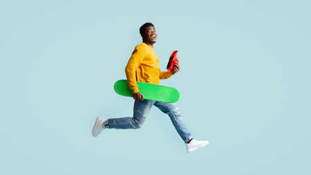 Emotional black guy running with skateboard towards copy spaceの写真素材