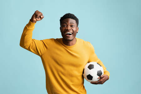 Emotional black guy with soccer ball posing on blueの写真素材