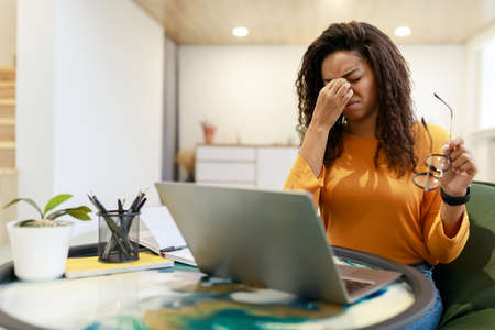 Eyes Strain. Overworked Young Black Woman Tired After Using Laptop Working Remotely On Computer At Home Office, Upset Lady Rubbing Nose Bridge, Taking Off Eyeglasses, Free Copy Spaceの写真素材