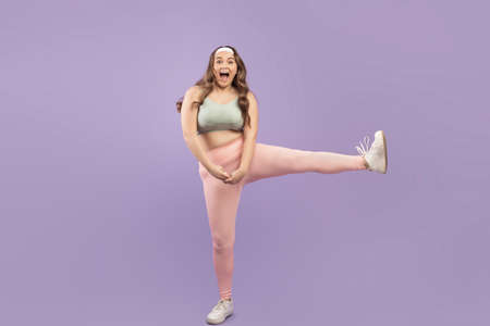 Funny glad young european plus size female athlete in sportswear with open mouth jumpsの写真素材