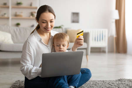Easy payments. Happy young mother and her child with laptop and credit card purchasing together online, free spaceの写真素材