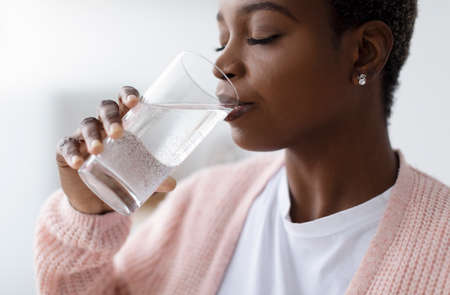 Millennial african american lady in casual drink water from glass in kitchen interior, profile,...