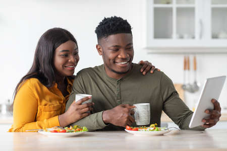 Young Black Couple Having Breakfast Together And Using Digital Tablet In Kitchenの写真素材