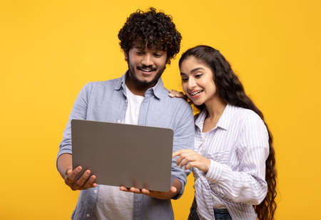 Online education, remote work and shopping. Happy indian couple looking at laptop, choosing purchase...