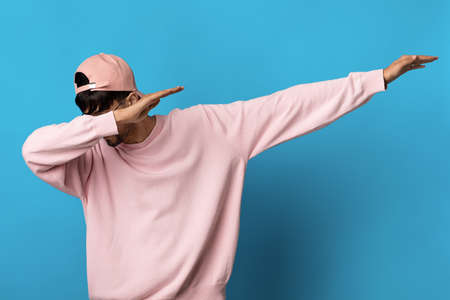 Millennial guy in pink sweatshirt and cap dabbing on blue backgroundの写真素材