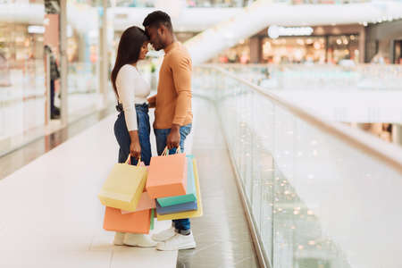 Cheerful young black couple hugging and holding shopping bagsの写真素材