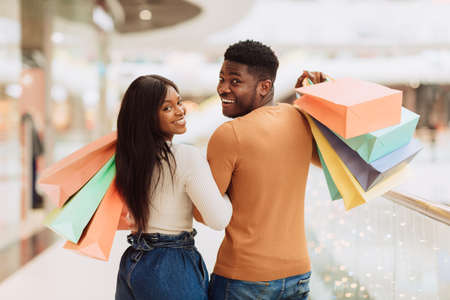 Portrait of happy black couple looking back holding shopping bagsの写真素材