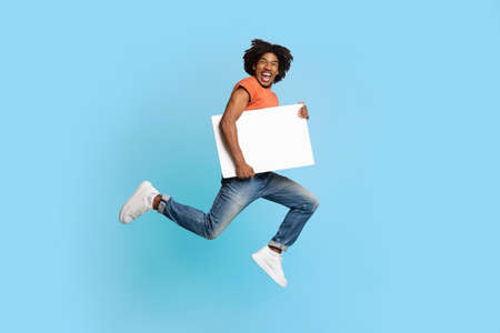 Happy african american guy running with empty placard for advertisement