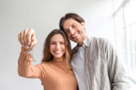 Satisfied glad young caucasian couple celebrate buying own apartment at loan, show keys in empty...